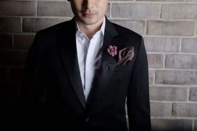 Close view of a black jacket with satin lapels, a flower lapel pin and a brown silk pocket square