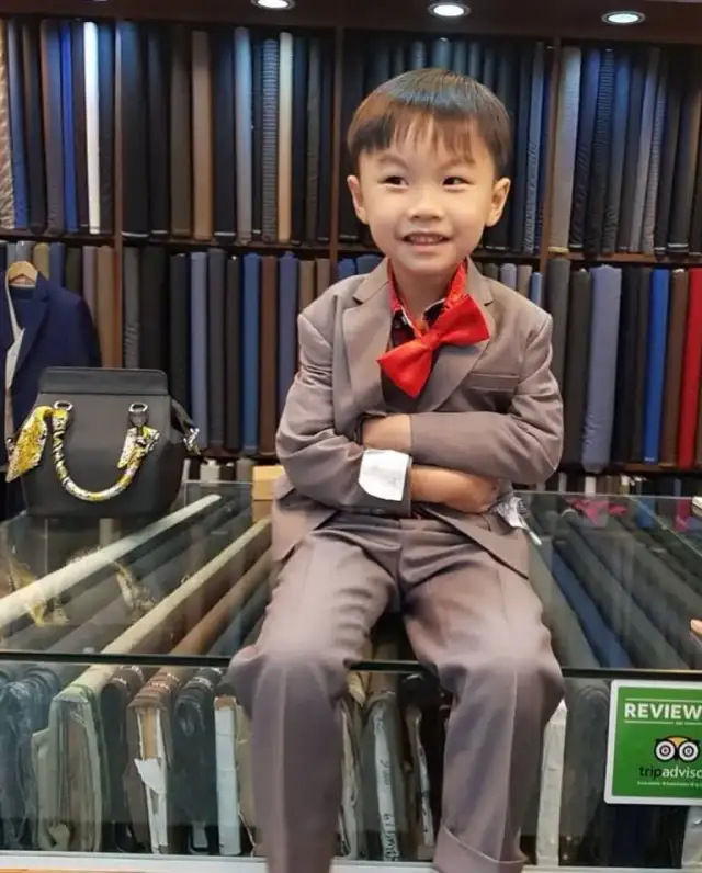 A boy in a tan suit and red bow tie seated in front of the fabric wall
