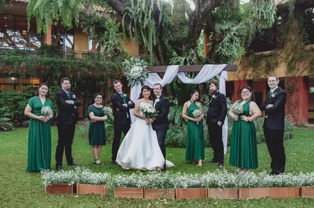 A bride and groom with bridesmaids in green and groomsmen in dark suits on a lawn