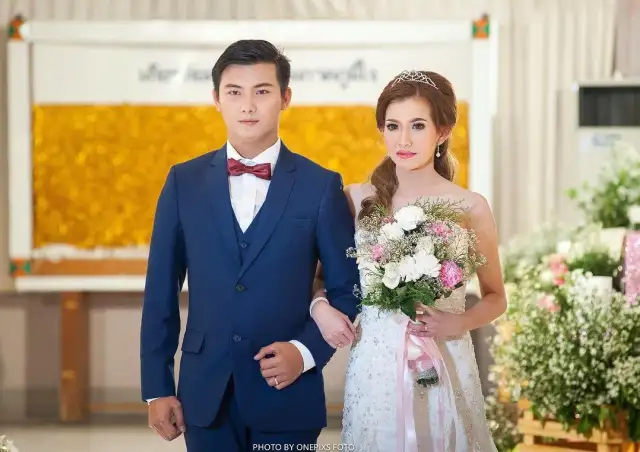 A bride and groom holding a bouquet, the groom in navy with a red bow tie