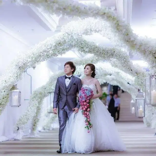 A bride and groom walking beneath an arch of white flowers