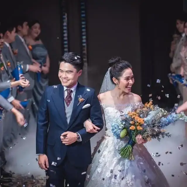 A bride and groom walking through falling confetti, the groom in a navy suit