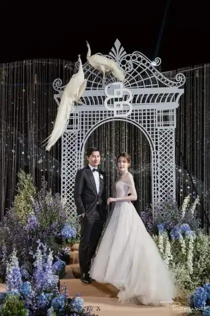 A bride and groom beside a white decorative gate hung with flowers