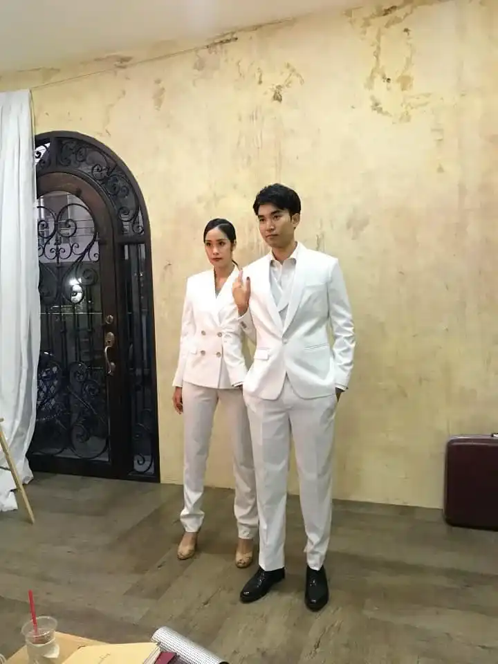 A couple in cream and white tailoring standing together indoors