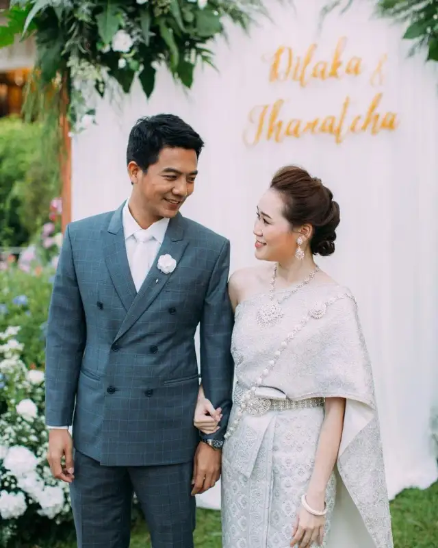 A couple in Thai wedding dress, the groom in a blue-grey double-breasted suit