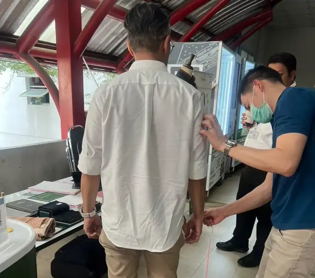 A fitting in progress beside the fabric wall, a tailor adjusting the client’s shirt