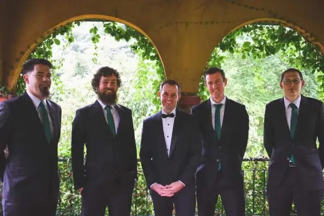 Five men in black tie standing under a garden arch