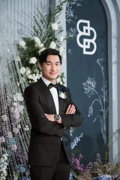 A groom in a black tuxedo standing beside a floral arrangement