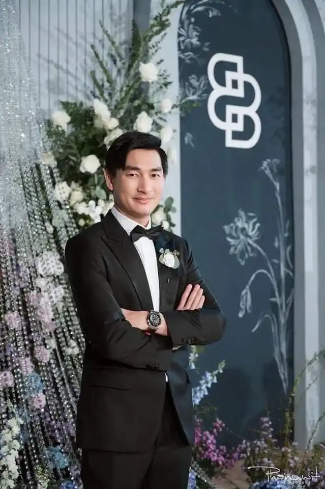 A groom in a black tuxedo standing beside a floral arrangement