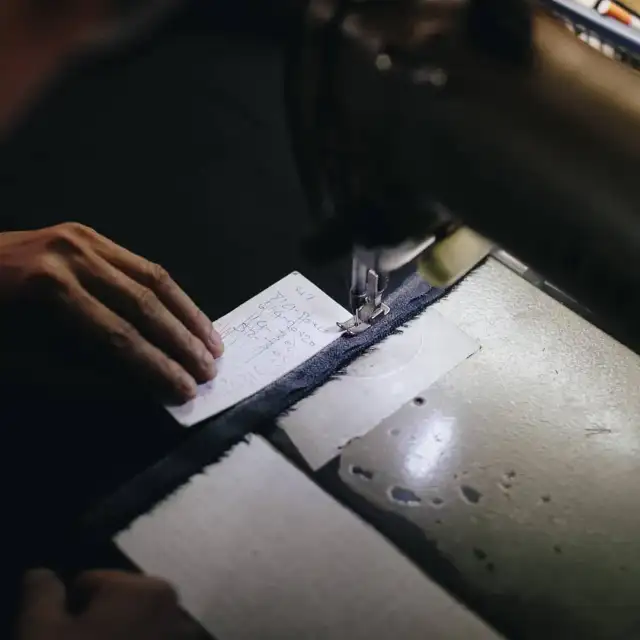 Hands marking cloth at the bench under a work lamp