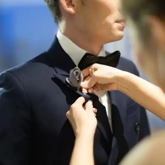 Hands tying a bow tie at the collar of a man in a navy dinner jacket