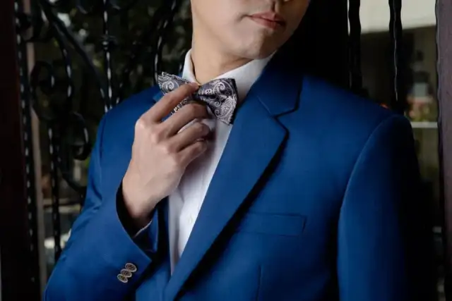 A man in a blue jacket adjusting a patterned bow tie at his collar