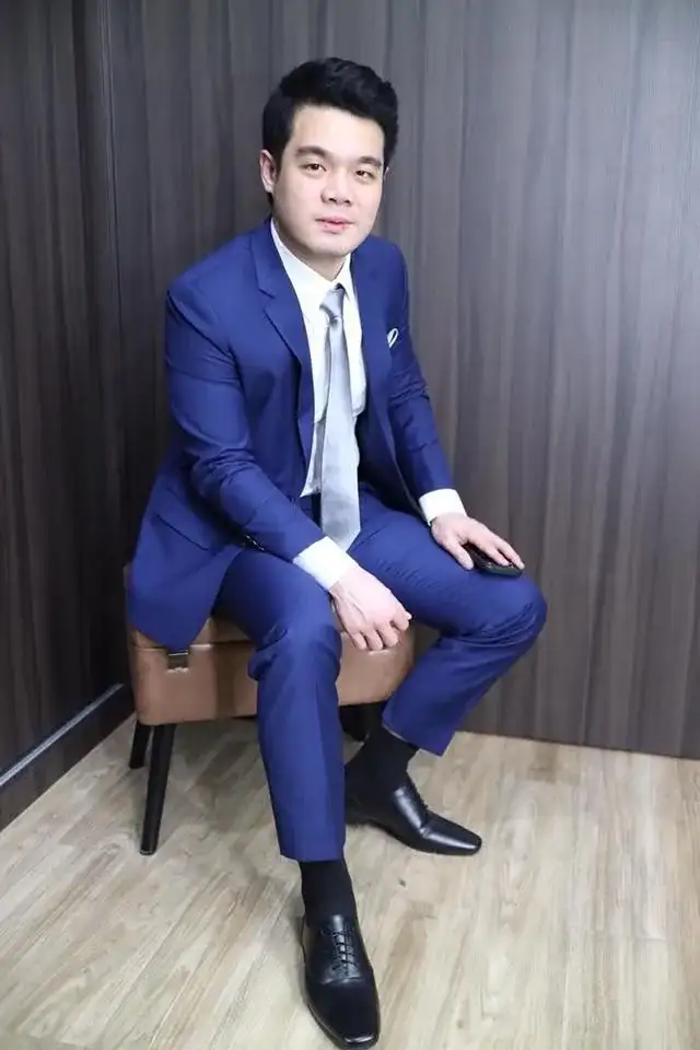 A man in a blue suit seated on a stool, trousers and shoes in view