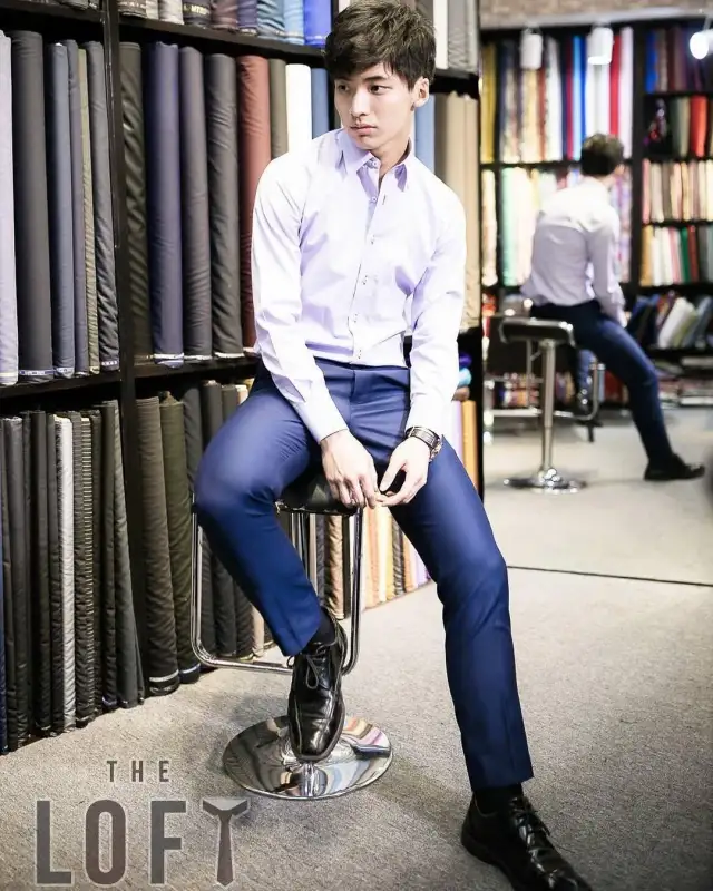 A man in a blue suit seated against the wall of rolled cloth