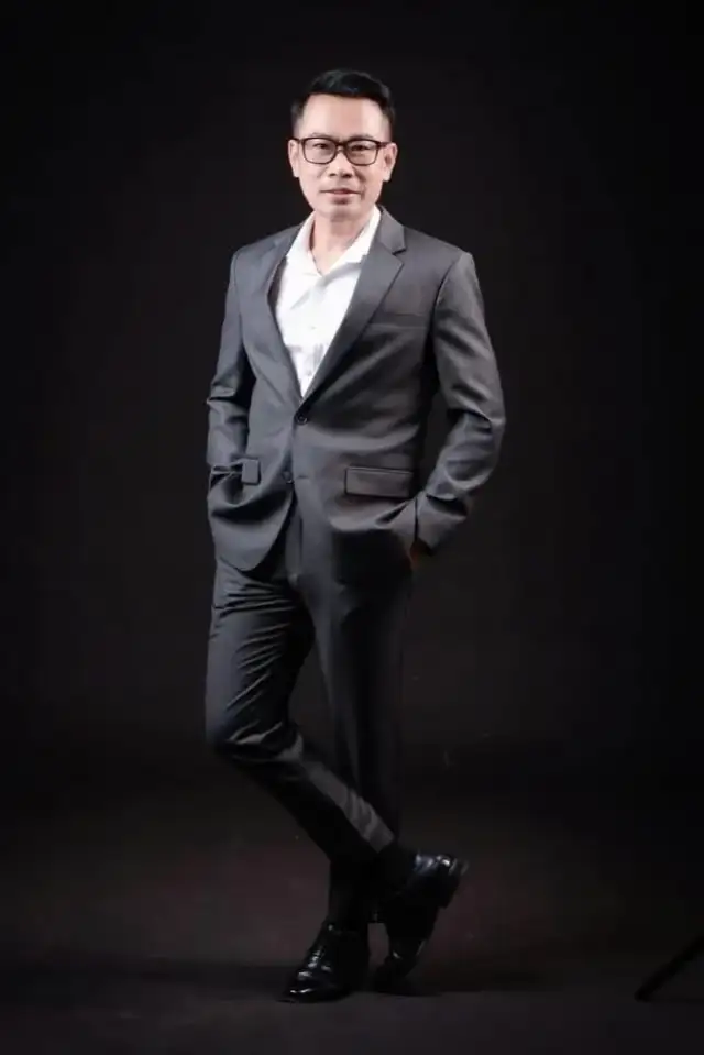 A man in a dark suit, full length against a black studio backdrop