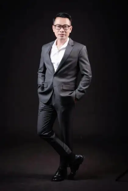 A man in a dark suit, full length against a black studio backdrop