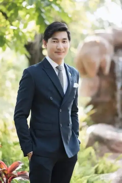 A man in a navy suit standing outdoors among greenery
