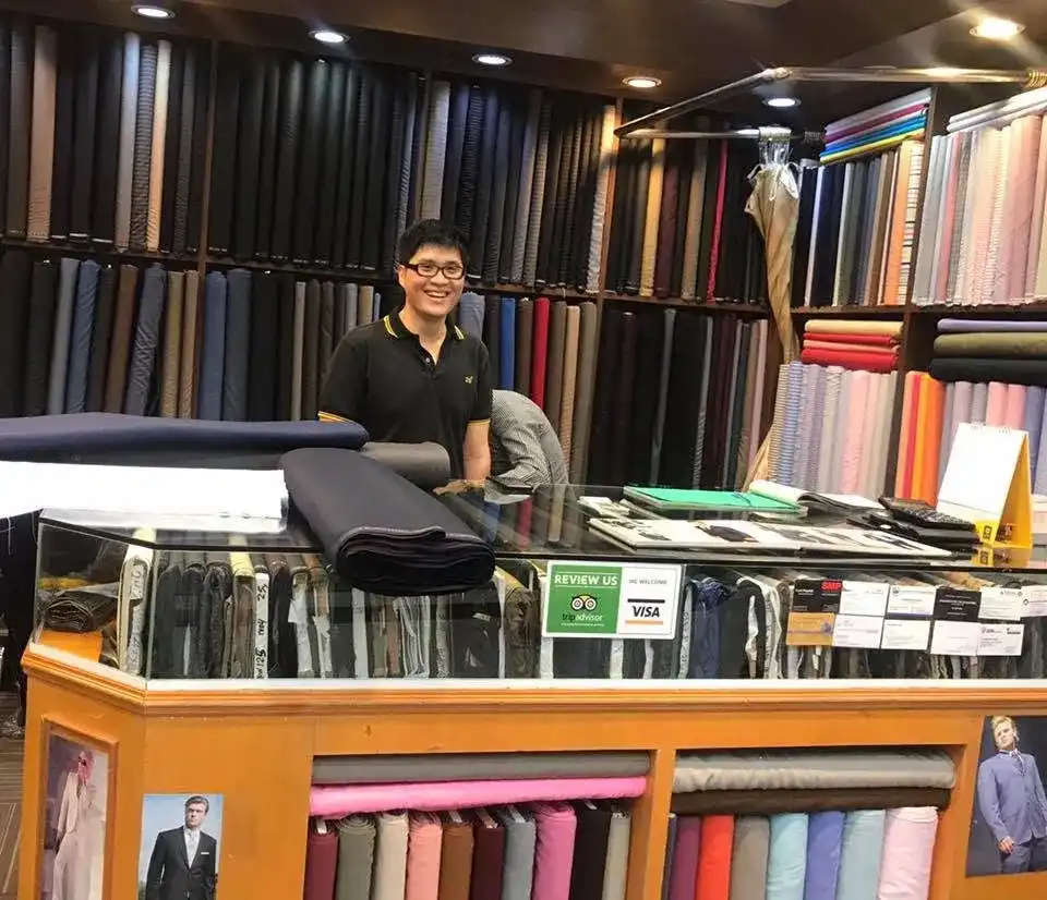 A man at the shop counter with rolls of cloth stacked behind him