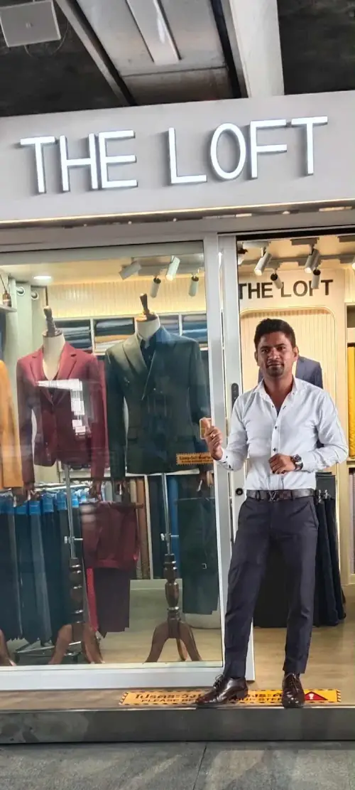 A man in a white shirt and navy trousers outside the shop window, suits on mannequins behind