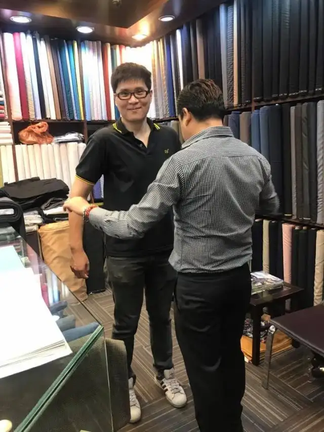 Two men shaking hands in the shop in front of the fabric wall