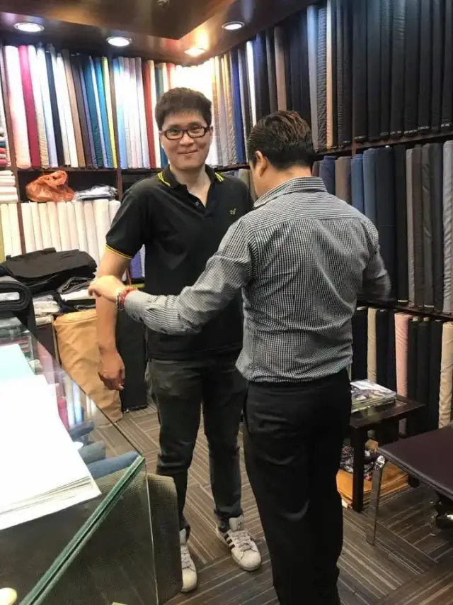 Two men shaking hands in the shop in front of the fabric wall