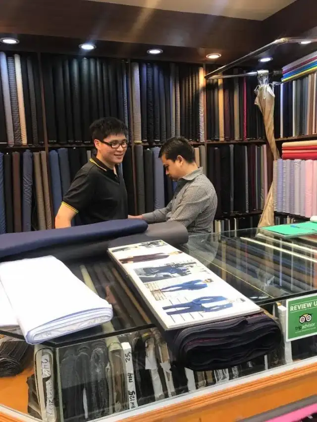 Two men working at the cutting table, shelves of folded cloth behind them