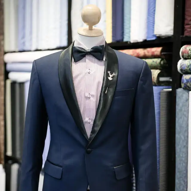 A navy dinner jacket with a shawl lapel on a mannequin in front of the fabric wall