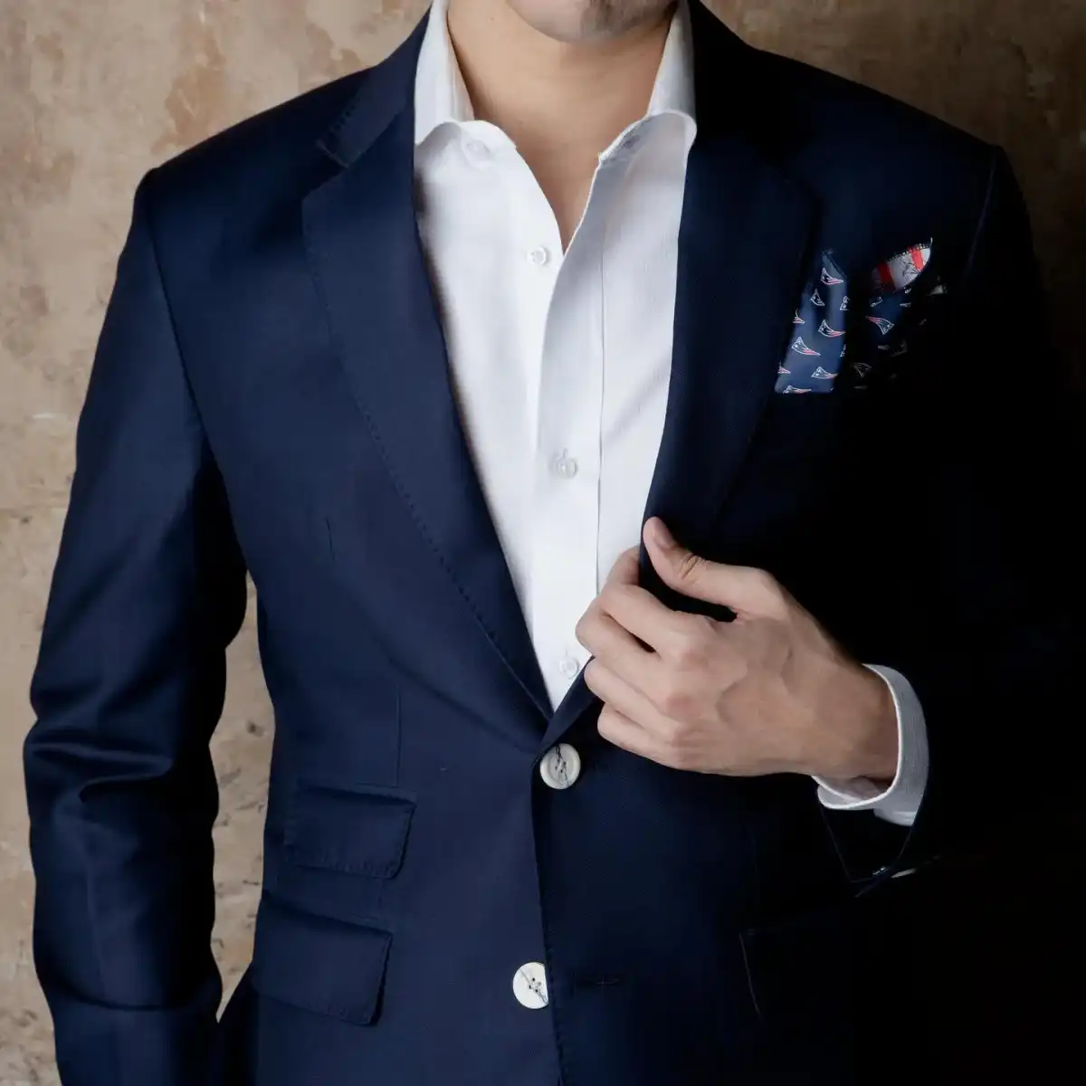A finished navy three-piece, the wearer’s hand at the button.