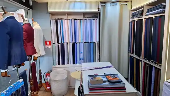 Inside the shop: mannequins in jackets, shelves of cloth and a table with books and a calculator