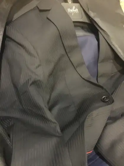 The shoulder and chest of an olive jacket hanging on a rail