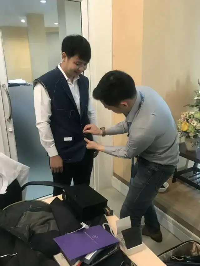 A tailor taking measurements over a client’s waistcoat during a fitting