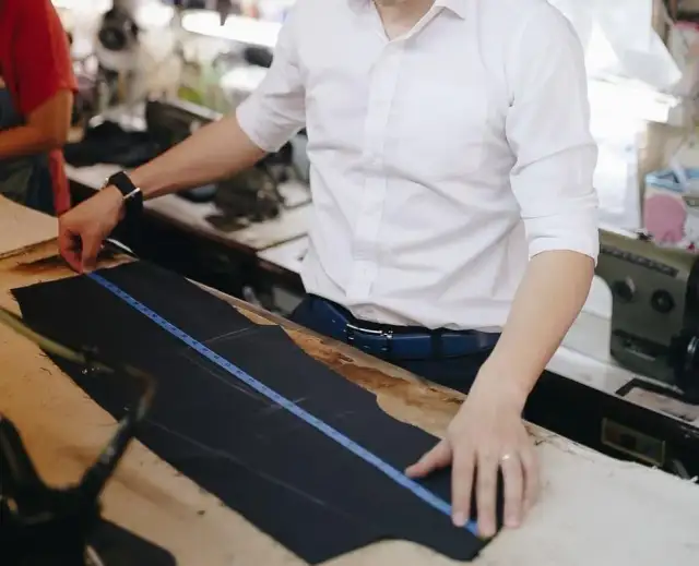 A tailor in a white shirt drawing a pattern on navy cloth with a long ruler