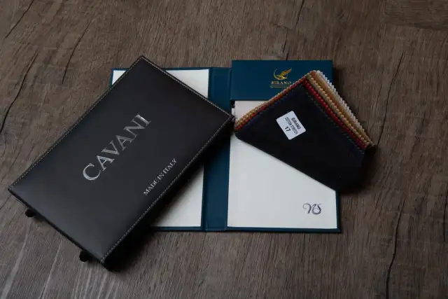 Three cloth books stacked on a wooden table, one black, one navy, one tan