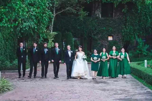 A wedding group photographed along a garden path, the bride at the centre