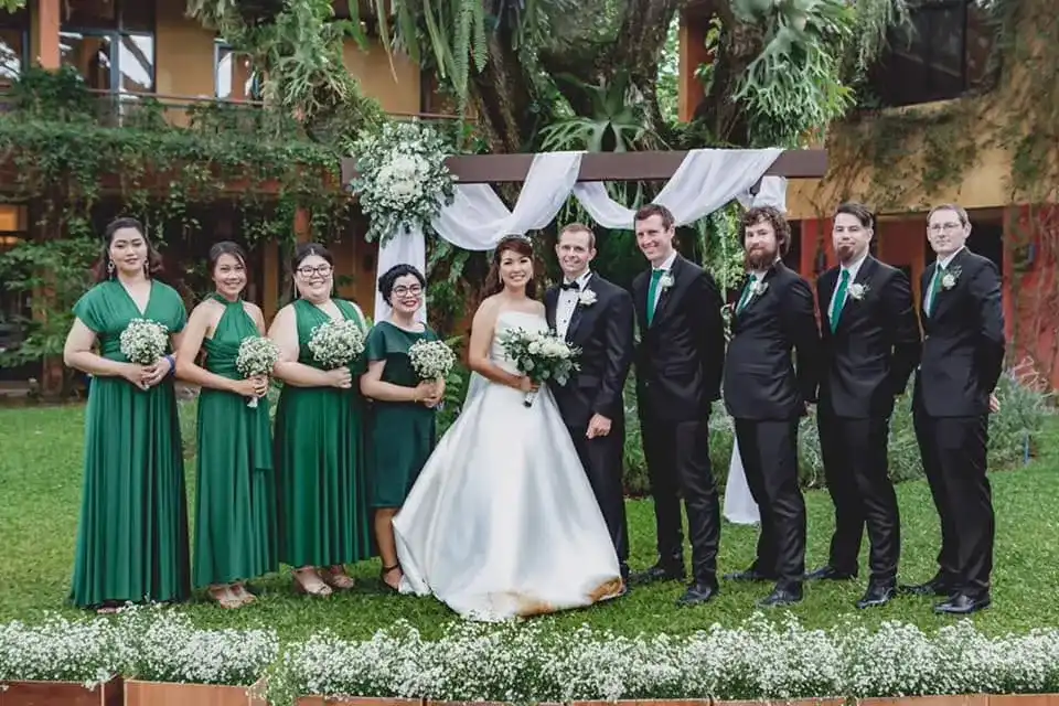 A wedding party posed on a lawn, the bride in white between her bridesmaids