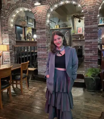 A woman in a grey layered outfit standing in a panelled interior