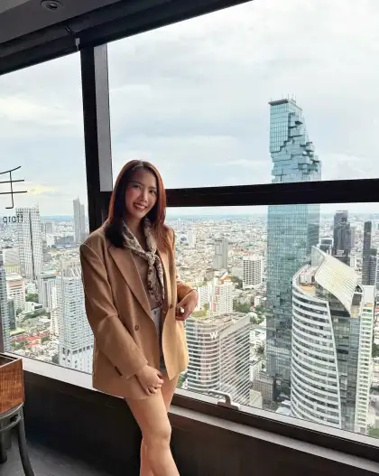A woman in a tan jacket standing at a window above the city