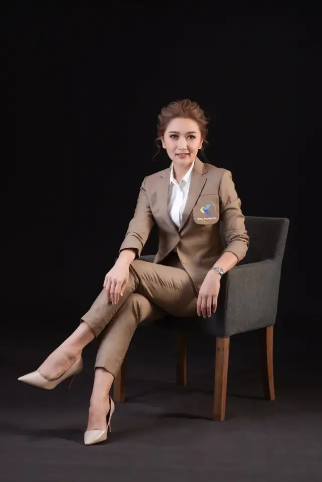 A woman in a tan suit seated in a chair, legs crossed